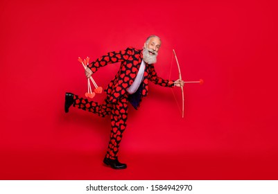 Full body profile photo of funky crazy aged guy cupid hobby love feelings couple shoot love bow arrow wear hearts pattern suit shirt tie pants shoes isolated bright red color background