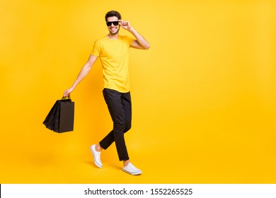 Full Body Profile Photo Of Handsome Guy Carry Boutique Bags Abroad Shopping Go Fashionable Mall Wear Casual T-shirt Black Pants Isolated Yellow Color Background