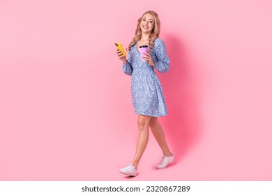 Full body profile photo of lovely lady use smart phone hold fresh coffee cup walking isolated on pink color background - Powered by Shutterstock