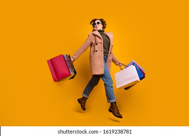 Full body profile photo of pretty shopper lady walk shopping center carry many packs wear sun specs casual pink coat pullover jeans leopard print shoes isolated yellow color background