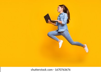 Full Body Profile Photo Of Pretty Business Lady Jump High Holding Notebook Hands Hurry Work Browsing Laptop Wear Casual Denim Outfit White Sneakers Isolated Yellow Color Background