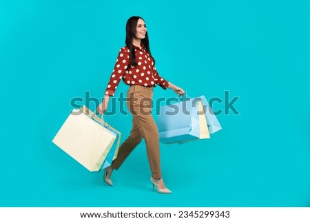 Full body profile photo of pretty lady hold boutique bags walking empty space isolated on teal color background