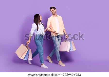 Full body profile photo of two cheerful friendly partners walk hold bags speak chatting empty space isolated on violet color background