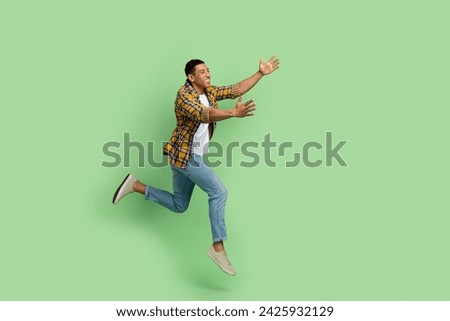 Full body profile portrait of carefree young man jump run arms catch empty space isolated on green color background