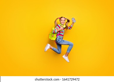 Full Body Profile Side Photo Kid Jump Run Fast Lesson Schoolgirl Hold Smartphone Headset Striped Sweater Denim Jeans Rucksack Bag Suspenders Overalls Isolated Bright Shine Yellow Color Background