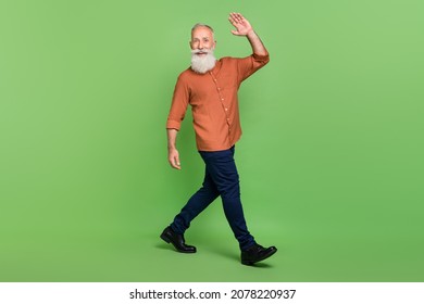 Full Body Profile Side Photo Of Senior Cheerful Man Go Walk Wave Arm Hello Isolated Over Green Color Background