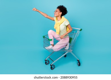 Full body profile side photo of young african cheerful girl have fun ride cart superhero isolated over blue color background