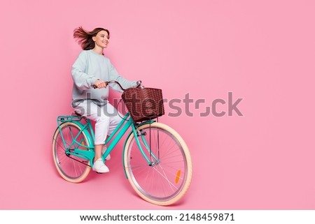 Full body profile side photo of young girl look empty space enjoy ride bike isolated over pink color background