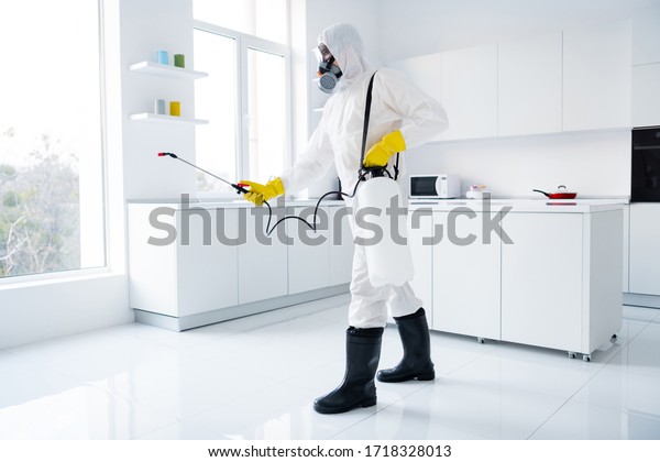 Full body profile side\
photo of focused guy cleaner in coverall spray sprayer window\
kitchen whitre surface prevent covid contamination epidemic\
spreading indoors house