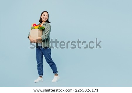 Full body profile young woman wear casual clothes hold brown paper bag with food products look aside on area isolated on plain blue background studio portrait. Delivery service from shop or restaurant