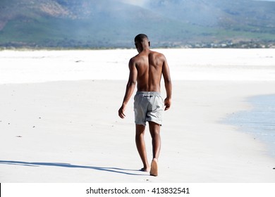 Full body rear view portrait of  shirtless young man walking barefoot on beach
