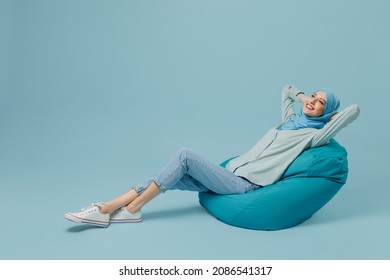 Full Body Relaxed Happy Cheerful Young Arabian Asian Muslim Woman In Abaya Hijab Sit In Bag Chair Isolated On Plain Blue Background Studio Portrait. People Uae Middle Eastern Islam Religious Concept