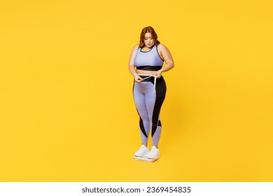 Full body sad young plus size big fat fit woman wear blue top warm up train stand on scales check result look at measure tape isolated on plain yellow background studio home gym. Workout sport concept - Powered by Shutterstock