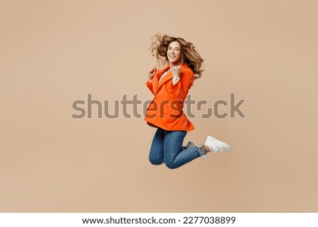 Full body satisfied fun young employee business woman corporate lawyer 30s wear classic formal orange suit glasses work in office jump high do winner gesture isolated on plain beige background studio