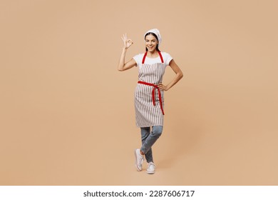 Full body satisfied happy young housewife housekeeper chef baker latin woman wear apron toque hat show ok okay gesture stand akimbo isolated on plain pastel light beige background. Cook food concept - Powered by Shutterstock