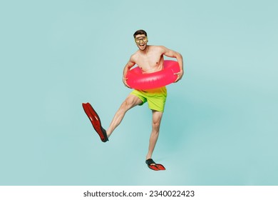 Full body satisfied young man wear green shorts swimsuit relax near hotel pool hold in hand inflatable rubber ring flippers isolated on plain blue background. Summer vacation sea rest sun tan concept