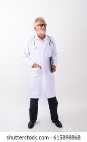 Full Body Shot Of Handsome Senior Bearded Man Doctor Standing And Thinking While Holding Clipboard Against White Background