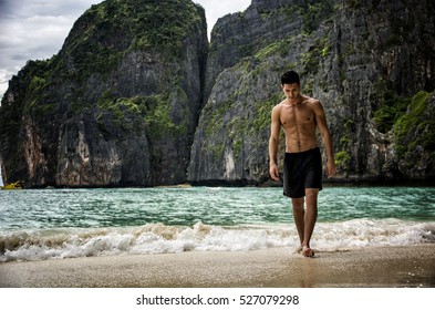 Full body shot of a handsome young man standing on a beach in Phuket Island, Thailand, shirtless wearing boxer shorts, showing muscular fit body