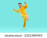 Full body shot of a happy, cheerful man wearing a trendy, stylish yellow suit and sunglasses having fun and dancing on a turquoise blue studio background. Party and fashion concept