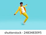 Full body shot of happy cheerful positive confident attractive young African American woman wearing stylish yellow party suit doing toe stand while dancing on blue studio background. Fashion concept