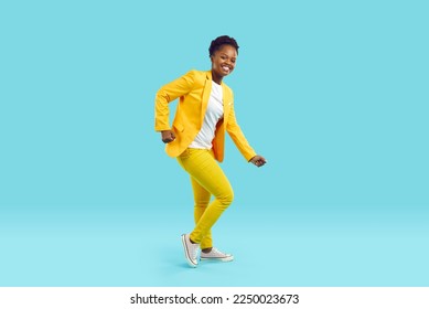 Full body shot of happy cheerful joyful beautiful young African American woman in bright yellow suit and white T shirt dancing isolated on blue color background. Fashion, party, having fun concept - Shutterstock ID 2250023673