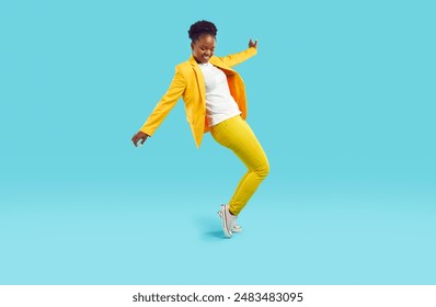 Full body shot of happy cheerful positive confident attractive young African American woman wearing stylish yellow party suit doing toe stand while dancing on blue studio background. Fashion concept - Powered by Shutterstock