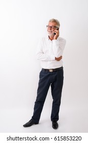 Full Body Shot Of Happy Senior Bearded Man Smiling While Thinking And Talking On Mobile Phone Against White Background