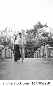 Full Body Shot Of Multi Ethnic Couple Standing Together And In Love On The Bridge Of Peaceful Green Park