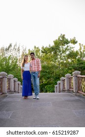 Full Body Shot Of Multi Ethnic Couple Standing Together And In Love On The Bridge Of Peaceful Green Park