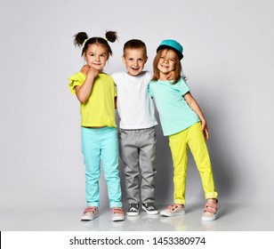 Full Body Shot Of Three Children In Bright Clothes, Two Girls And One Boy. Triplets, Brother And Sisters. Laughing And Screaming Loud Have Fun In The Studio