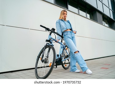 Full body shot, trendy girl with her electric bicycle , modern building in the back 