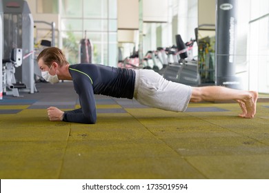 Full Body Shot Of Young Man With Mask Doing Plank Position On The Floor At Gym During Corona Virus Covid-19