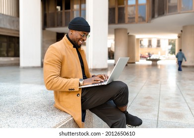 Full Body Side Portrait Black Businessman In Elegant Stylish Clothing Sitting On Steps In City Smiling And Using Computer Laptop.