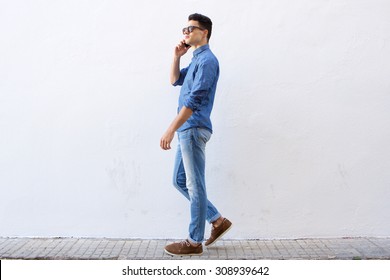 Full Body Side Portrait Of A Handsome Young Man Walking And Talking On Cell Phone