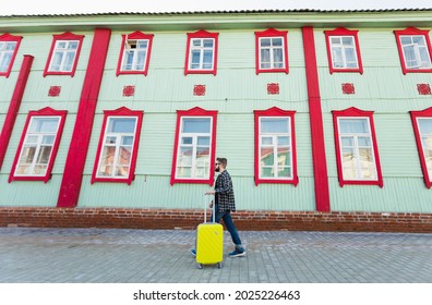 Full Body Side Portrait Of Happy Travel Man With Suitcase Walking Along The Building In City.