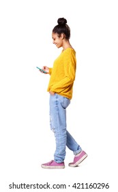 Full Body Side Portrait Of Relaxed Young Woman Walking And Reading Text Message On The Mobile Phone Over White Background
