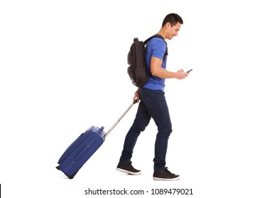 Full body side portrait of smiling mature man walking with suitcase and cellphone on white background