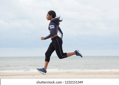 Full Body Side Portrait Of Sporty Young Black Woman Running By The Beach