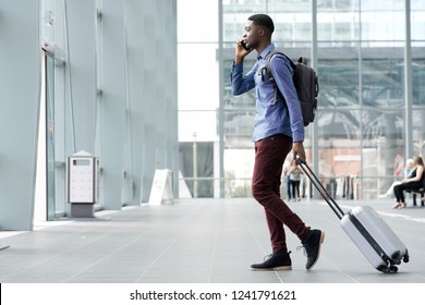 Full body side portrait of young african man traveling with suitcase and cellphone at airport 