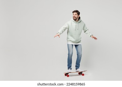 Full body side profile view fun young excited amazed happy smilign caucasian man wearing mint hoody riding skateboard isolated on plain solid white background studio portrait. People lifestyle concept - Powered by Shutterstock