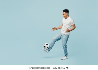 Full body side profile view happy cheerful young man fan wearing t-shirt cheer up support football sport team hit soccer ball on leg watch tv live stream isolated on plain pastel blue color background - Powered by Shutterstock