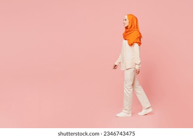 Full body side profile view smiling young arabian asian muslim woman wear orange abaya hijab walk go strolling look aside isolated on plain pink background. Uae middle eastern islam religious concept - Powered by Shutterstock