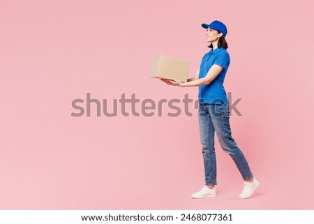 Full body side profile view delivery girl employee woman wear blue cap t-shirt uniform workwear work as dealer courier hold give cardboard box walk go isolated on plain pink background Service concept