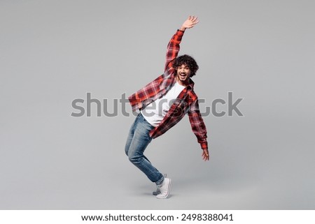 Full body side profile view young happy smiling Indian man wearing red shirt casual clothes stand on toes lean back with outstretched hands isolated on plain grey color background. Lifestyle concept