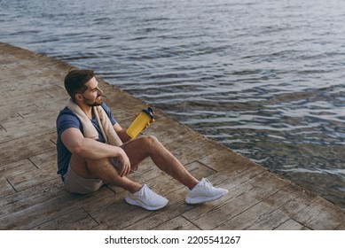 Full body side top view young strong sporty fit sportsman man in sports clothes towel warm up training drink water hold bottle at sunrise over sea beach outdoor on pier seaside in summer day morning - Powered by Shutterstock