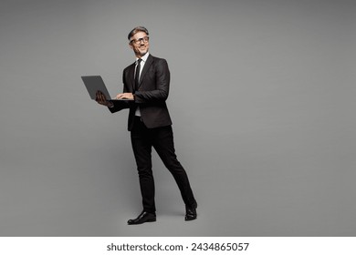 Full body side view adult employee IT business man corporate lawyer wears classic formal black suit shirt tie work in office hold use laptop pc computer look aside isolated on plain grey background - Powered by Shutterstock