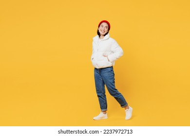 Full body side view cheerful young woman of Asian ethnicity wear white padded windbreaker jacket red hat walk go look aside on workspace isolated on plain yellow background People lifestyle concept - Powered by Shutterstock