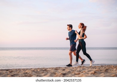 Full body side view couple young two friends strong sporty sportswoman sportsman woman man in sport clothes warm up training run on sand sea ocean beach outdoor jog on seaside in summer day morning - Shutterstock ID 2042537135