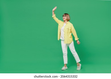 Full body side view elderly smiling happy fun caucasian friendly woman 50s in glasses yellow shirt walking go waving hand isolated on plain green background studio portrait People lifestyle concept - Powered by Shutterstock