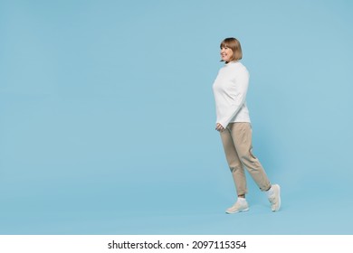 Full Body Side View Elderly Smiling Cheerful Fun Caucasian Woman 50s Wear White Knitted Sweater Walking Going Stroll Isolated On Plain Blue Color Background Studio Portrait. People Lifestyle Concept